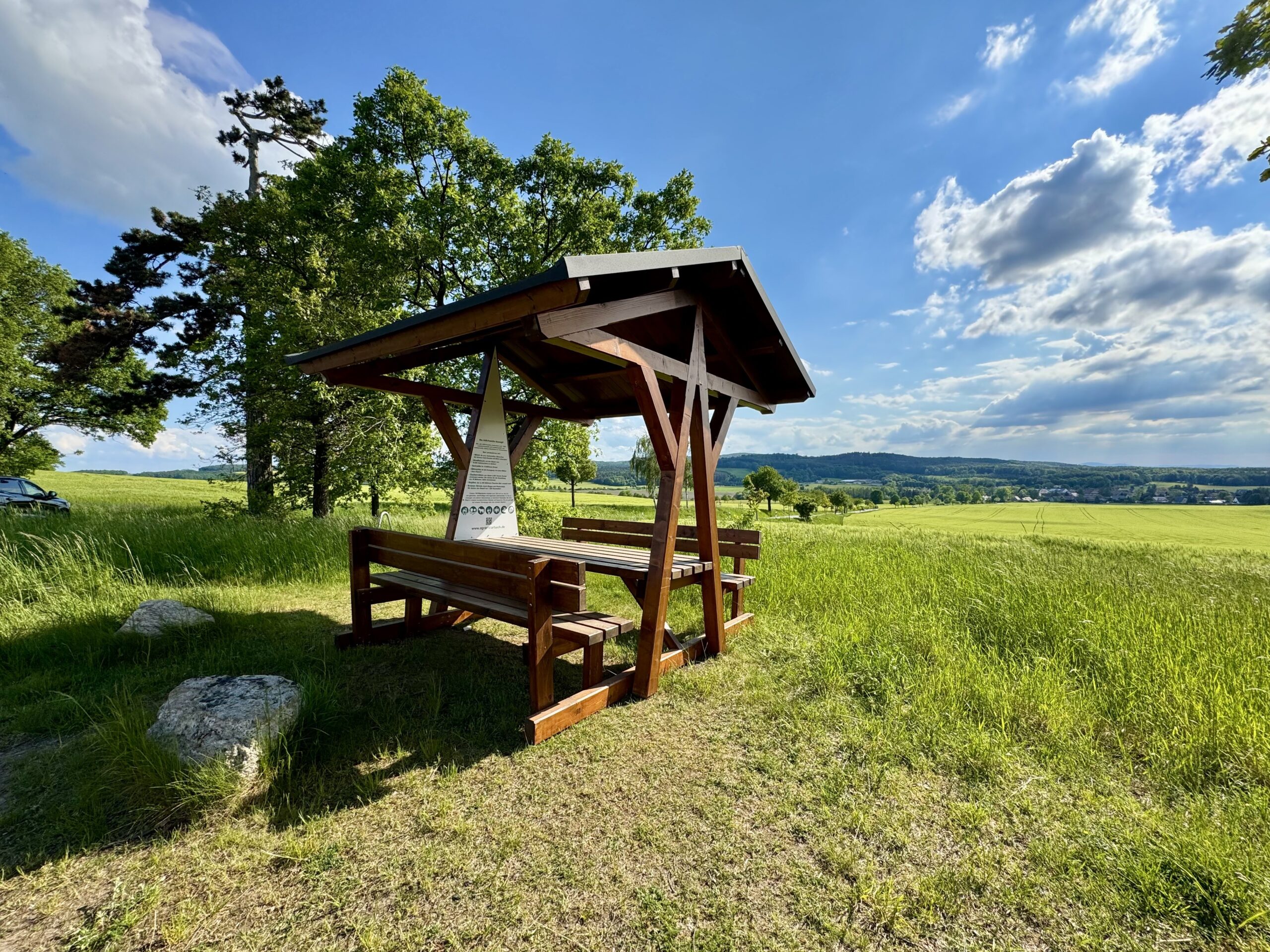 Zu sehen ist eine überdachte Sitzgelegenheit auf dem Heideberg mit Blick auf Wiesa und die Königshainer Berge. Links im Bild erkennt man die Schwarzkiefer.